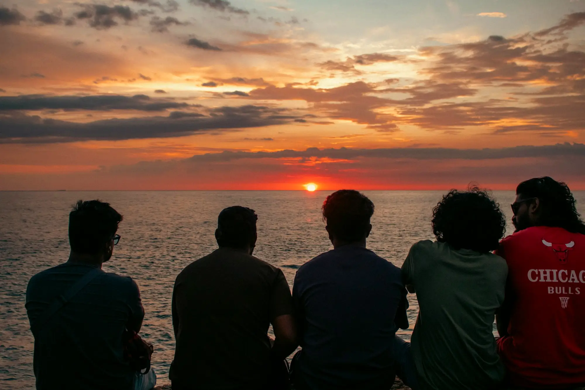 Cinq amis assis côte à côte face au coucher de soleil sur la mer